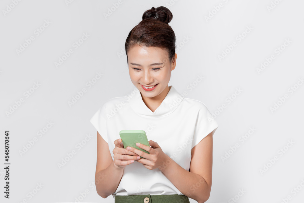 Happy young woman writing message on smartphone isolated against white wall Happy young woman writing message on smartphone isolated against white wall