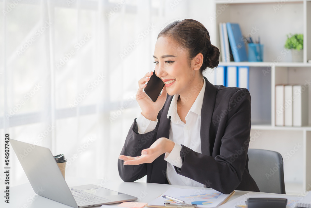 Young beautiful asian woman using smartphone and working with laptop while sitting at office desk, working from home concept. Young beautiful asian woman using smartphone and working with laptop while sitting at office desk, working from home concept.