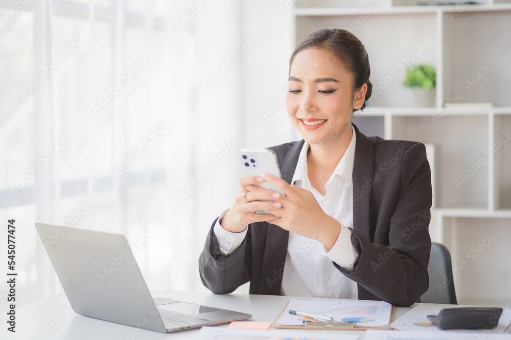 Young beautiful asian woman using smartphone and working with laptop while sitting at office desk, working from home concept. Young beautiful asian woman using smartphone and working with laptop while sitting at office desk, working from home concept.