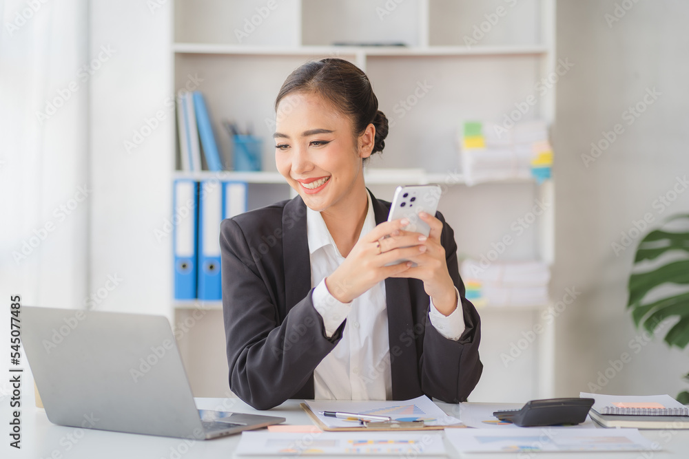 Young beautiful asian woman using smartphone and working with laptop while sitting at office desk, working from home concept. Young beautiful asian woman using smartphone and working with laptop while sitting at office desk, working from home concept.