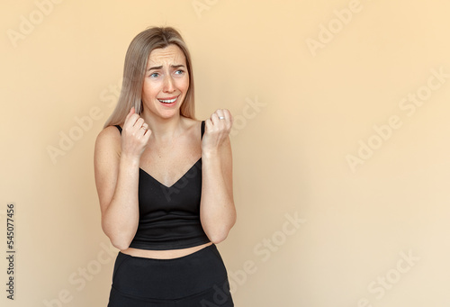 I'm afraid. Fright. Portrait of the scared young woman with freckles. Worried girl wearing casual black clothes standing over beige background with copy space