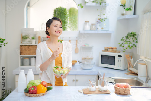 .Young woman eating fresh salad in modern kitchen.