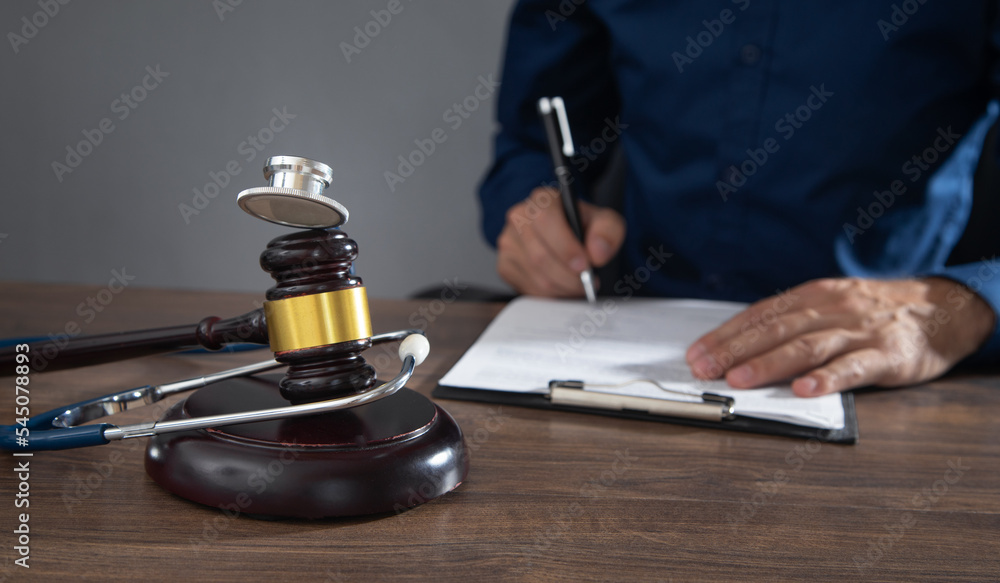 Man signing in document. Judge gavel and stethoscope on the table Man signing in document. Judge gavel and stethoscope on the table