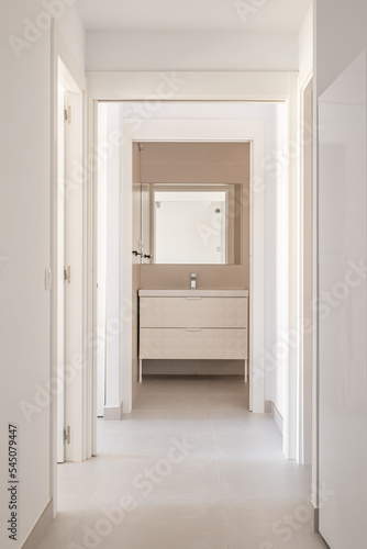 Bright corridor with white walls and tiled floor with a doorway to the bathroom