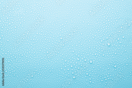Water drops on cold soft light blue background as pattern of tiny glossy shine drops as dew, texture, top view.