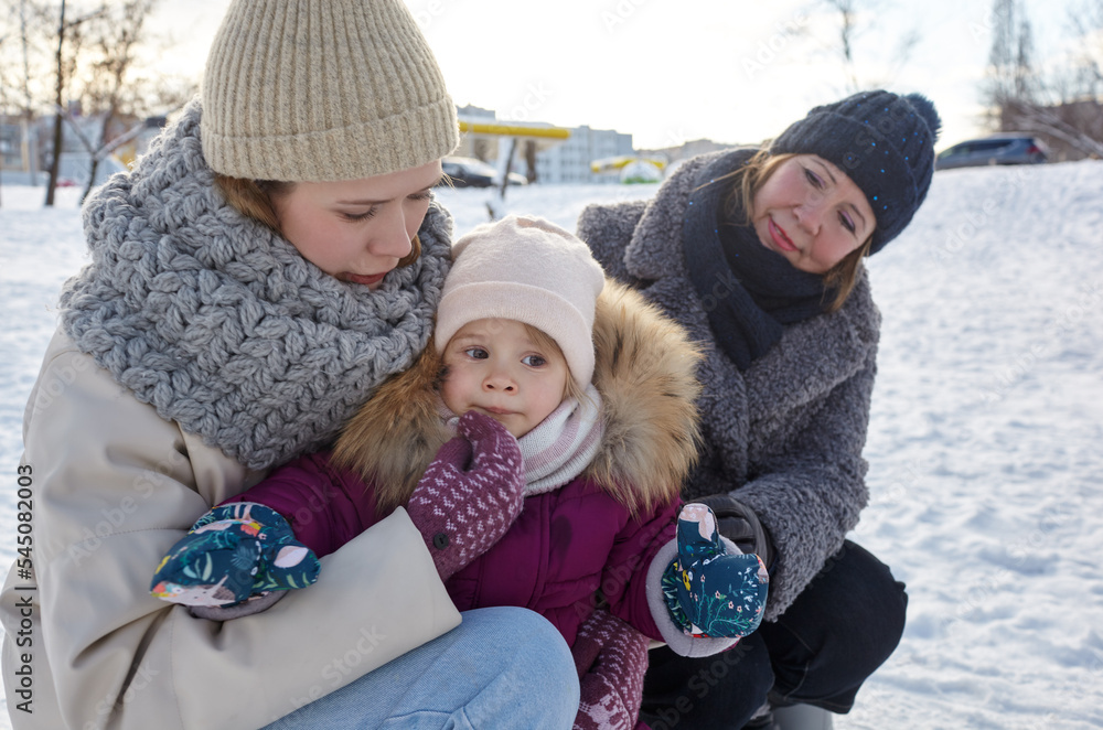 Fototapeta premium Grandmother, mother and daughter are walking in the winter city park on Christmas and New Year holidays. Parent and little child having fun outdoors