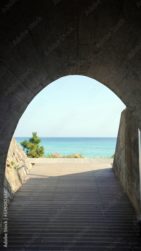 A tunnel with a view of the blue sea wooden deck that waves through the blue sky