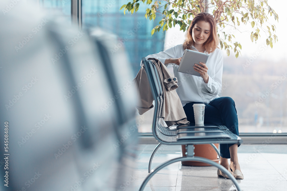 Young smiling woman using a tablet in the departure hall at the airport.