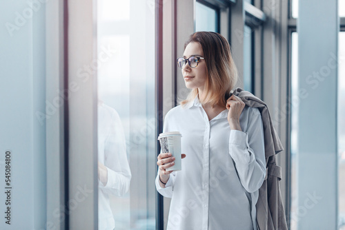 Obraz na płótnie Young woman standing at the window of a modern business center with a cup of coffee. w salonie
