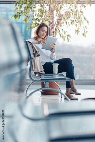 Obraz na płótnie Young traveling woman using a tablet and waiting for a flight in the departure hall at the airport. w salonie