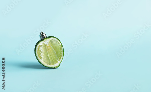 stylish creative new year layout with a green lime
 in the shape of a Christmas ball  on a pastel blue background. new year food concept or creative postcard. copy space