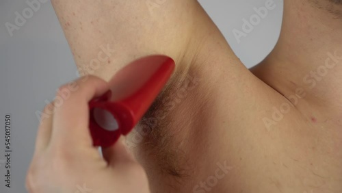 A young man smears antiperspirant on his hairy armpits. Man supports body positivity. Long hair in the armpits.
