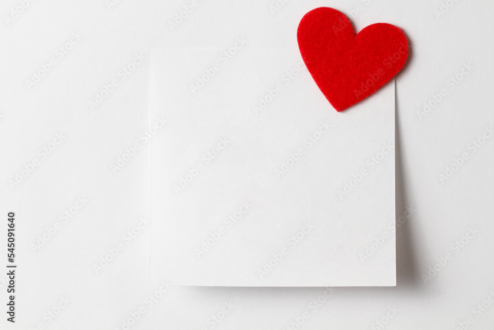 Close-up of a short white note paper with a red heart. Valentines Day background. Copy for writing text. Concept of recognition of love, romantic relationships, Happy Valentine's day Close-up of a short white note paper with a red heart. Valentines Day background. Copy for writing text. Concept of recognition of love, romantic relationships, Happy Valentine's day