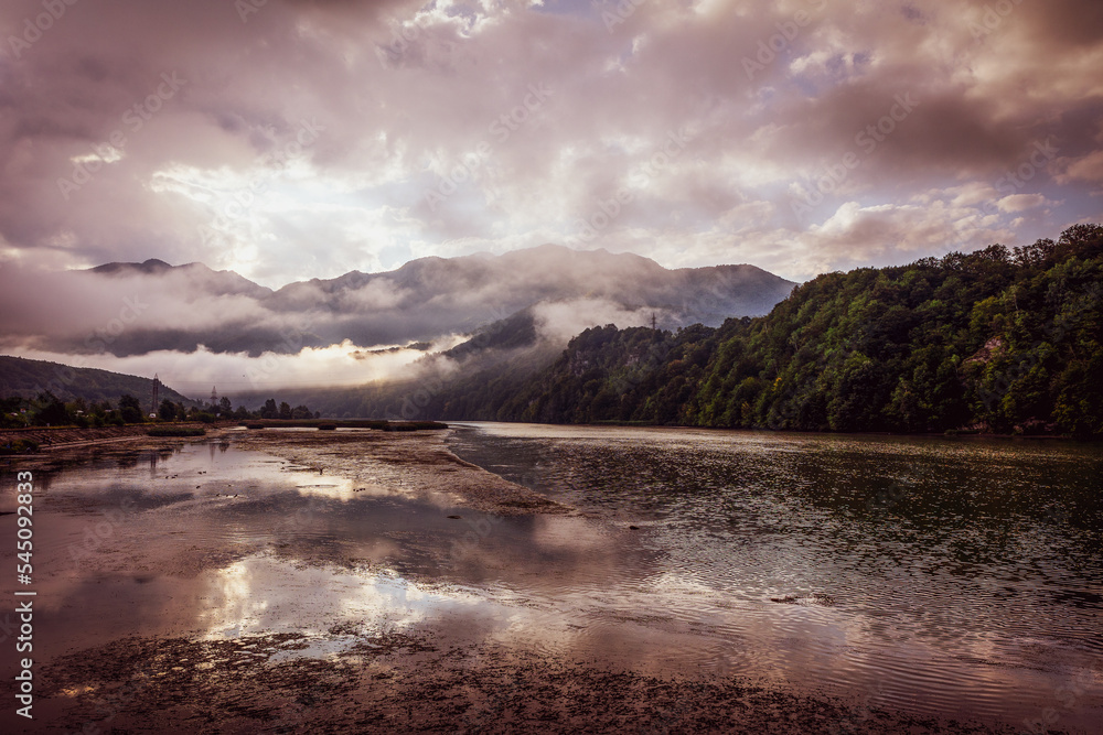 A beautiful mountain landscape with fog and slow flowing river.