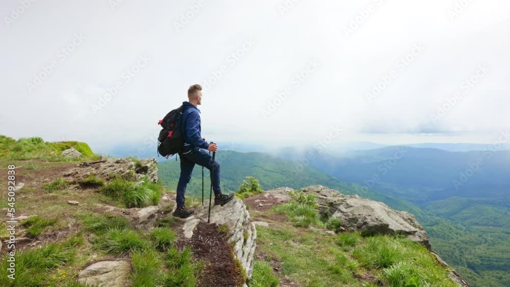 Back view of young male hiking, standing on rock, hill. Sporty man wearing backpack, looking forward, enjoying nature, view, having rest, relaxing. Concept of tourism and hiking. Back view of young male hiking, standing on rock, hill. Sporty man wearing backpack, looking forward, enjoying nature, view, having rest, relaxing. Concept of tourism and hiking.