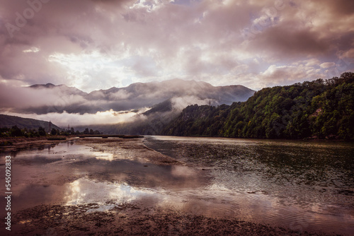 A beautiful mountain landscape with fog and slow flowing river.