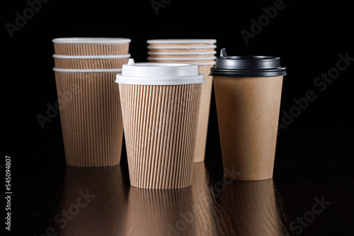 Several disposable paper cups with lids of different types and sizes for drinks on a black background. Side view.