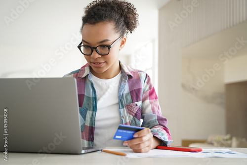 African american young girl holding credit card makes payment uses online banking services on laptop
