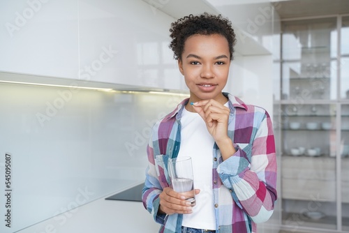 Mixed race young girl takes pills, vitamins, dietary supplement for wellness holding glass of water