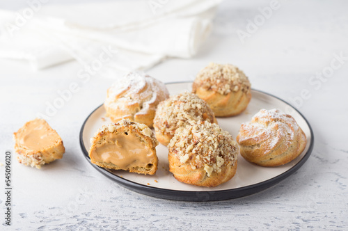 Gluten-free oat profiteroles with caramel cream of boiled condensed milk, sprinkled with powdered sugar and nuts on a light blue background. Delicious homemade food photo