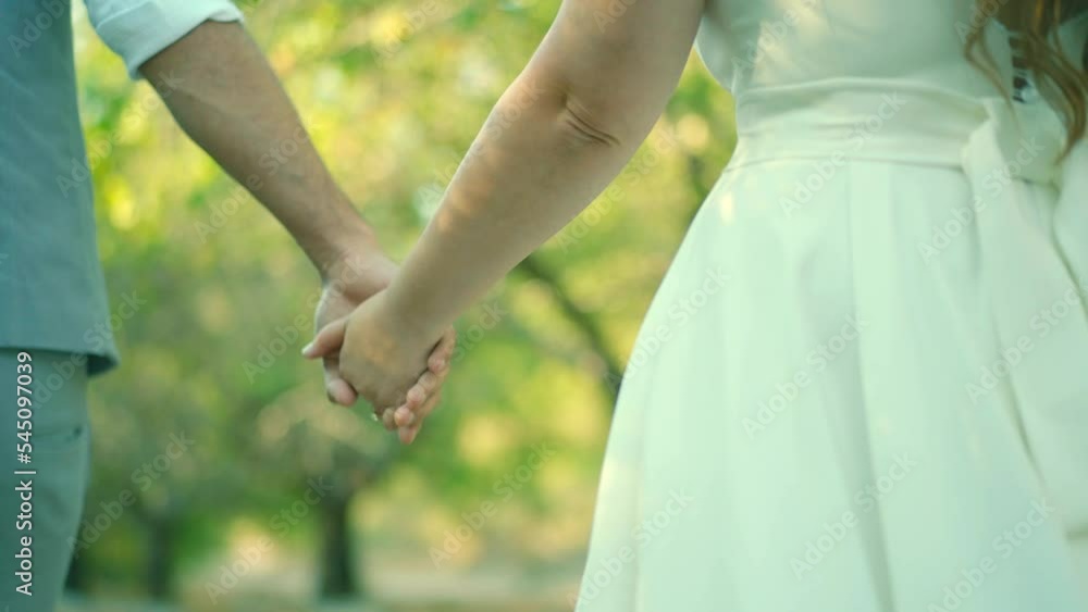 Bride and groom walking hand in hand in a garden. High quality FullHD footage