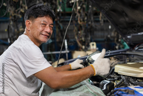 Asian mechanic man wearing gloves and thumbs up working and fixing car in auto repair shop, Car Mechanic Concept
