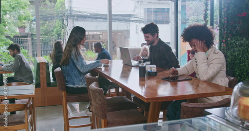 Group of people inside coffee shop. Female friend handing espresso to male colleague sitting at cafe restaurant table. Men and women customers together at cafe place