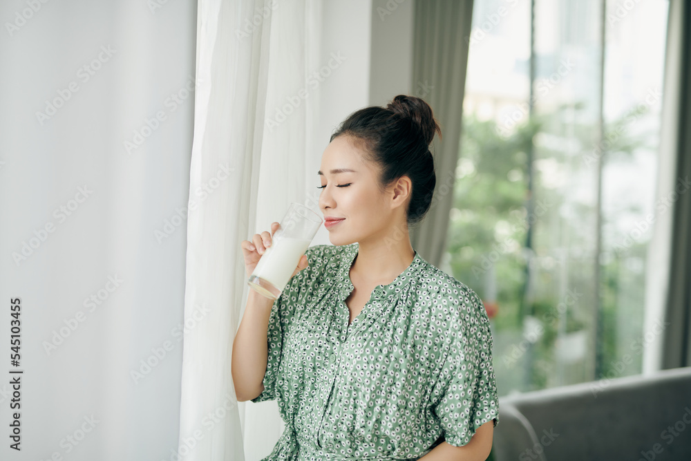 Happy young Asian woman drinking milk from the glass in the living room at home Happy young Asian woman drinking milk from the glass in the living room at home