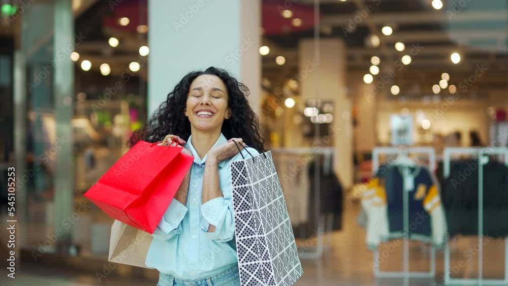 Portrait of cheerful young shopaholic woman holding paper bags with purchases and smiling at camera standing on shopping center. Happy lady shopping on black friday joyfully jumps for joy enjoys Portrait of cheerful young shopaholic woman holding paper bags with purchases and smiling at camera standing on shopping center. Happy lady shopping on black friday joyfully jumps for joy enjoys