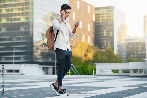 Phone, music and city with a man student walking to university or college during his morning commute. Headphones, social media and 5g mobile technology with a male pupil in an urban town for a walk
