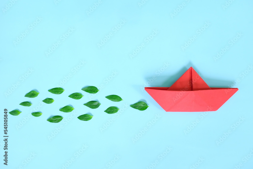 Clean energy for sea travel and sustainable maritime transport concept. Paper boat emitting fresh green leaves as footprint.