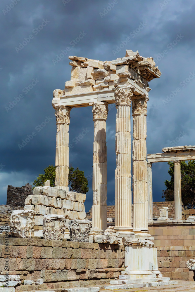 The ruined Temple of Trajan in Pergamon Ancient City. Corinthian order stone-cut relief on the frieze. Dramatic sky at background. History, art or architecture concept. Bergama, Turkey The ruined Temple of Trajan in Pergamon Ancient City. Corinthian order stone-cut relief on the frieze. Dramatic sky at background. History, art or architecture concept. Bergama, Turkey