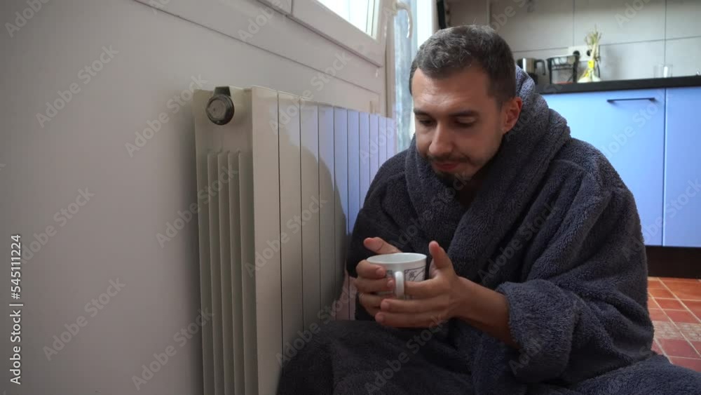 A man with a cup of hot drink in a warm bathrobe sits by a cold radiator. No gas A man with a cup of hot drink in a warm bathrobe sits by a cold radiator. No gas