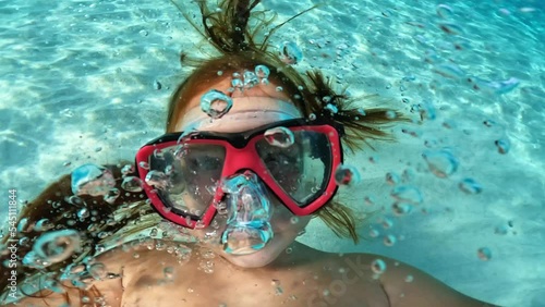 Underwater selfie of young red hair girl with diving mask holding camera while having fun in crystalline turquoise sea water. Slow motion