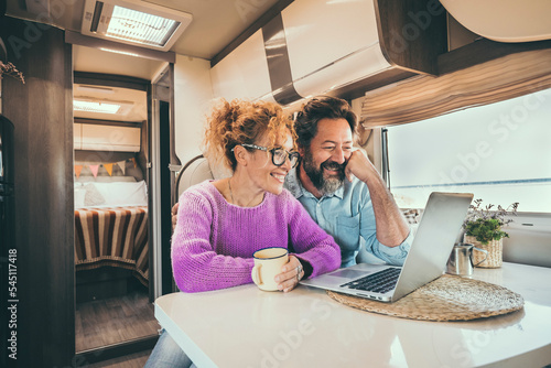 Man and woman using laptop inside camper van during travel lifestyle van life. Happy couple smile in front of a computer during rv motor home vacation. Smart working and digital nomad concept day