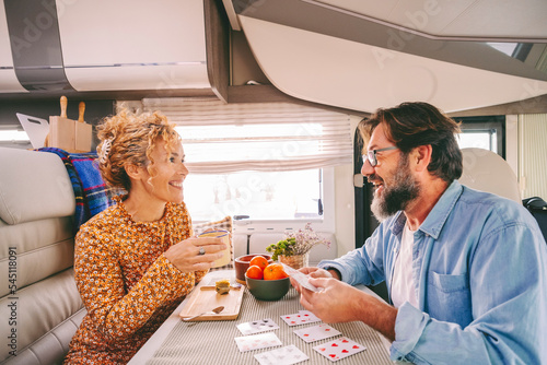 One happy couple enjoy time and have fun together inside camper van during travel lifestyle or holiday with vehicle. Man and woman playing cards with smile and joy.. Indoor leisure activity people