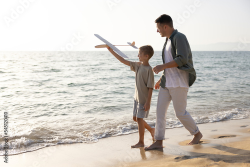 Father and son walking barefoot along the seashore with a handmade wooden plane