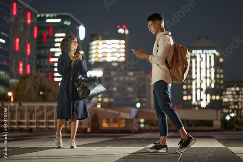 Business people, phone and city at night, social media and order transport with online app in New york. Man and woman workers leaving urban town late after work day with 5g mobile smartphone on web