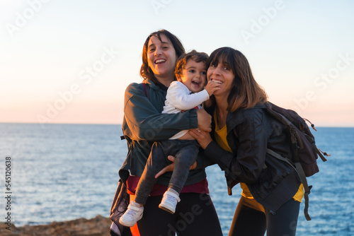 Aunt of the child and mother hugging with him child on the coast by the sea at sunset
