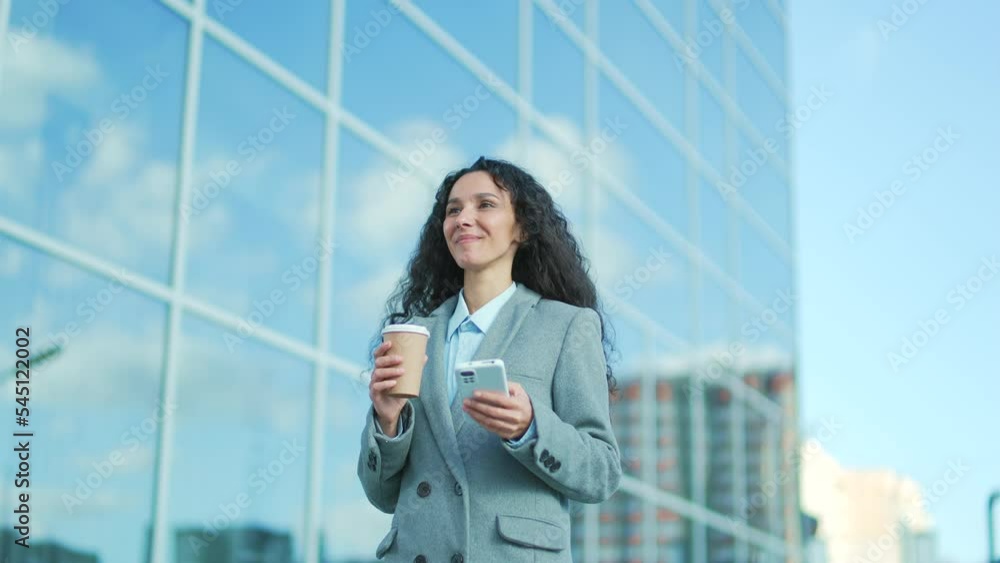 young hispanic business woman employee walking on a city street background office building with a smartphone and coffee cup in hand Female uses mobile phone browsing typing chatting outside outdoors young hispanic business woman employee walking on a city street background office building with a smartphone and coffee cup in hand Female uses mobile phone browsing typing chatting outside outdoors