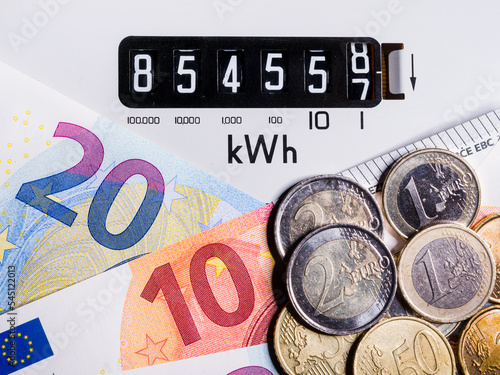 Close-up of electric meter and Euro notes and coins. Focus on kWh symbol. Concept for global energy crisis, cost of living, high electricity prices, meter reading and higher bills.