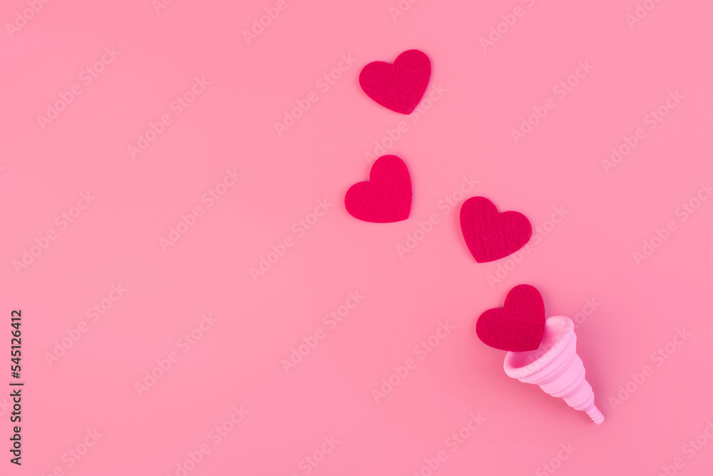 Silicone pink menstrual cup flatlay. Women's health and alternative hygiene. Cup with drops of blood or red hearts on a pink background. eco-friendly, Alternative reusable product for female hygiene.