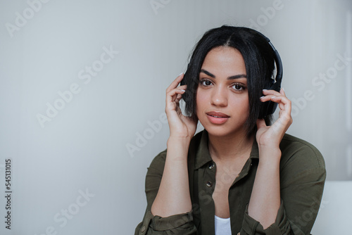 Close up African American young woman in headphones looking at camera holding headset having break. Brazilian woman enjoying music at home. Adorable happy student. Musician at studio, youth.