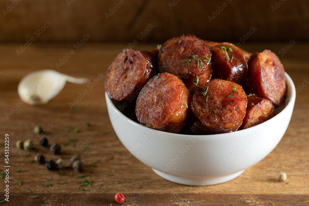 Slices of smoked pork sausages in a bowl on wood Slices of smoked pork sausages in a bowl on wood