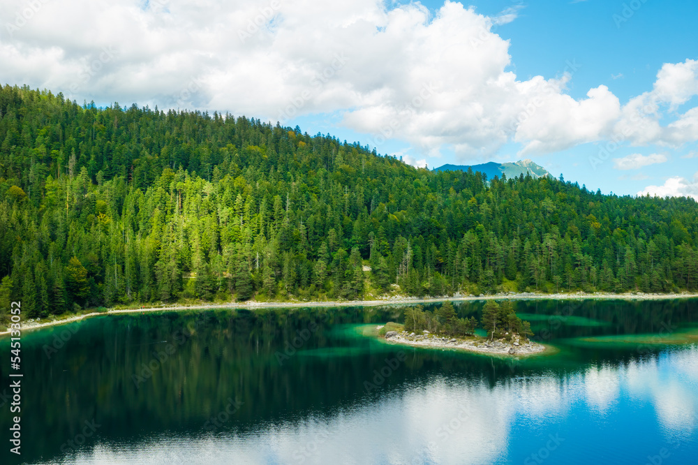 Mountains with spruce trees and clouds are reflected in a forest river. Summer landscape of a riverside. 