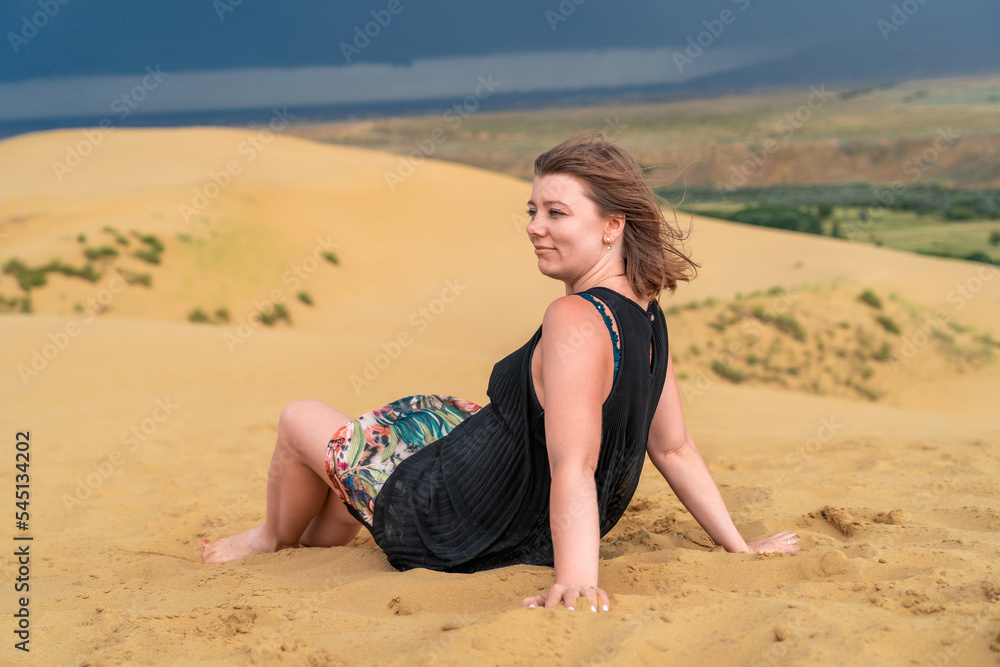 Carefree woman in dress sitting in sand dunes Carefree woman in dress sitting in sand dunes