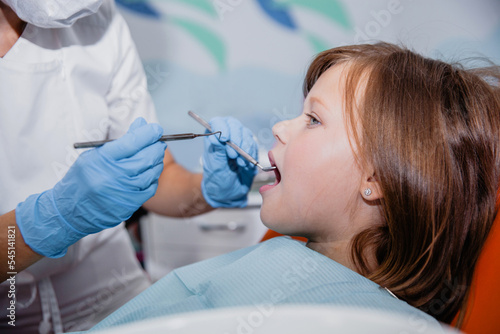 A woman dentist in a white coat and and blue gloves treats the teeth of European appearance girl in a dental office