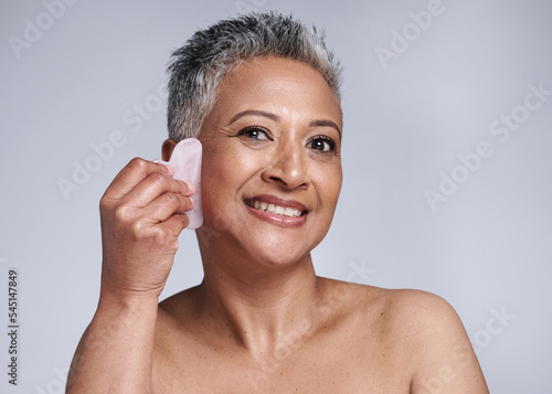 Portrait, happy and senior woman gua sha, face and smile in grey studio background. Elderly woman, skincare model and wellness care of healthy skin with facial treatment with beauty cosmetic tool