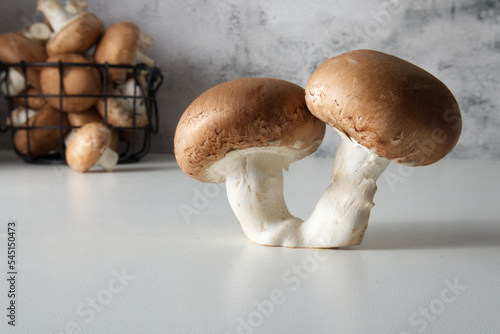 Two brown cap champignons on the table close-up against the background of a basket with mushrooms