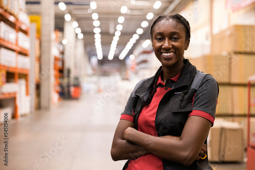 Smiling saleswoman with arms crossed standing in warehouse at hardware store